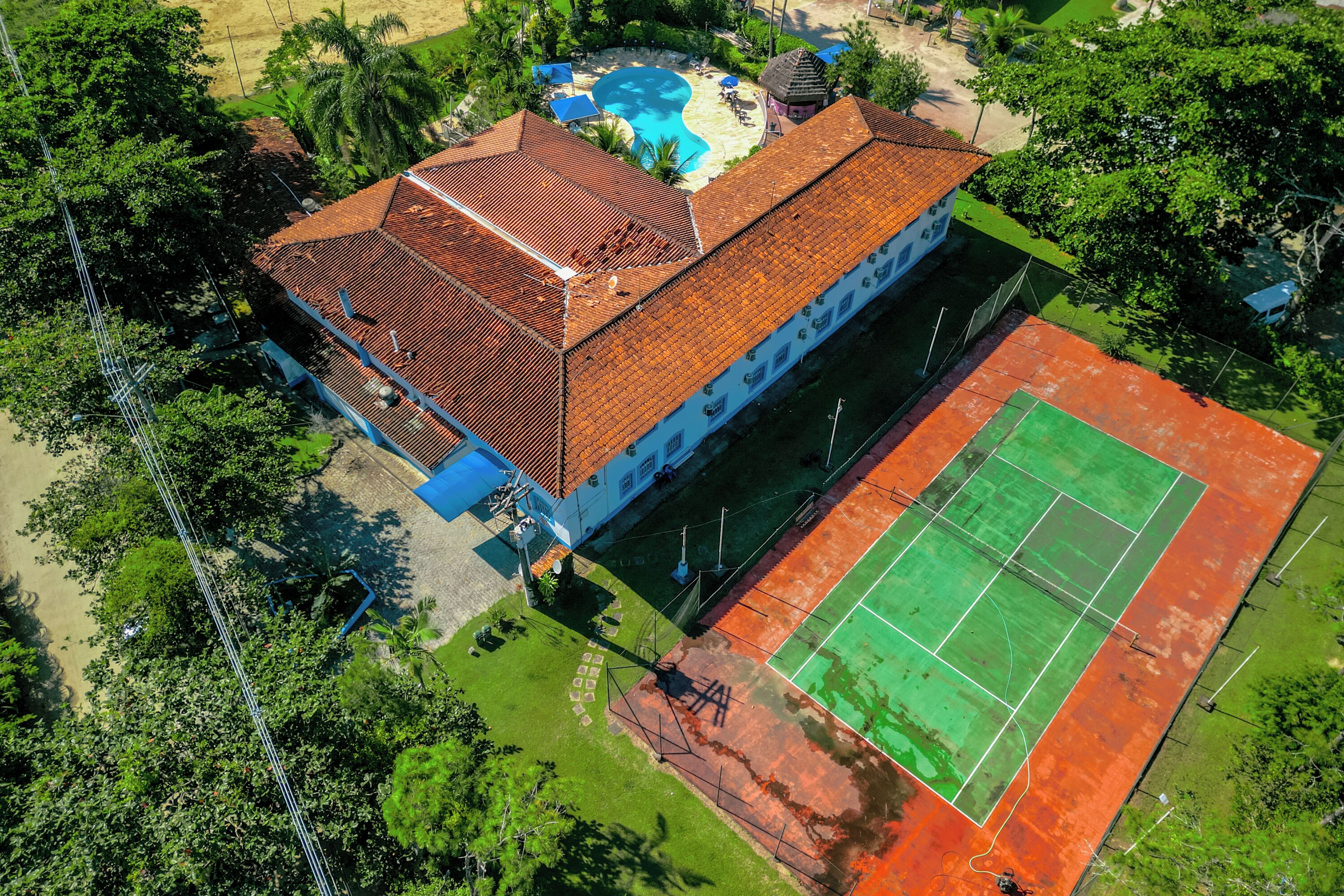 Vista aérea de un edificio con piscina, cancha de tenis y zonas verdes circundantes.