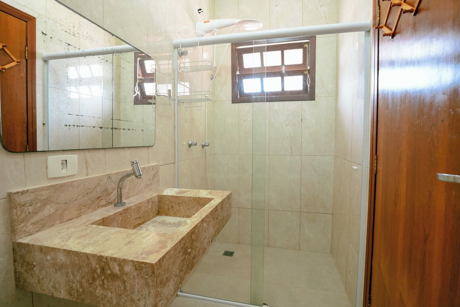 A bathroom with a marble sink, a mirror, a shower with a glass door, and a wooden door.