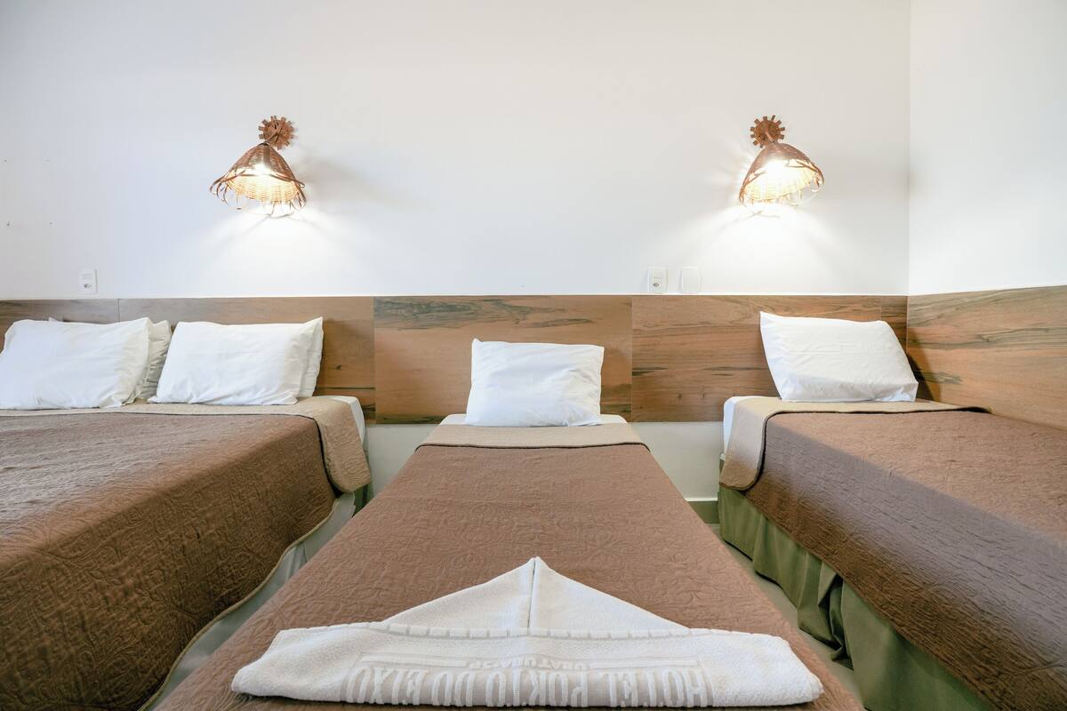 Habitación de hotel con dos camas, cada una con colcha marrón y almohadas blancas. Hay dos lámparas de pared de diseño único.