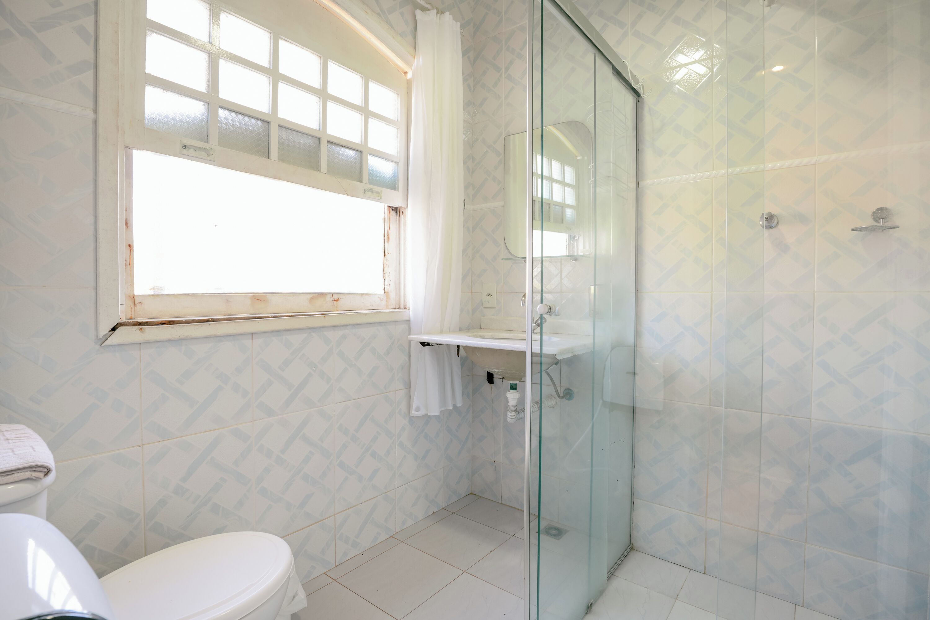 A bathroom with a toilet, a sink, a glass shower enclosure, and a window with a curtain.