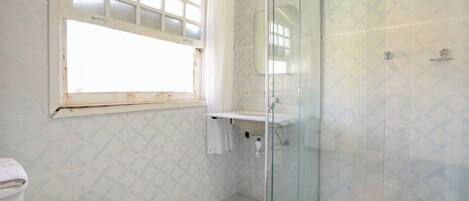 A bathroom with a toilet, a sink, a glass shower enclosure, and a window with a curtain.