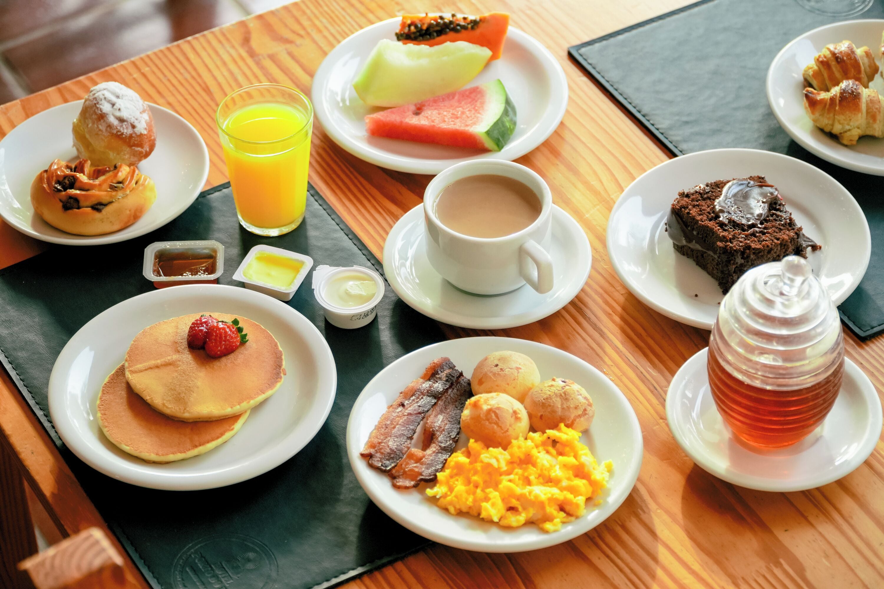 A breakfast buffet with pancakes, eggs, bacon, toast, pastries, and fruit.