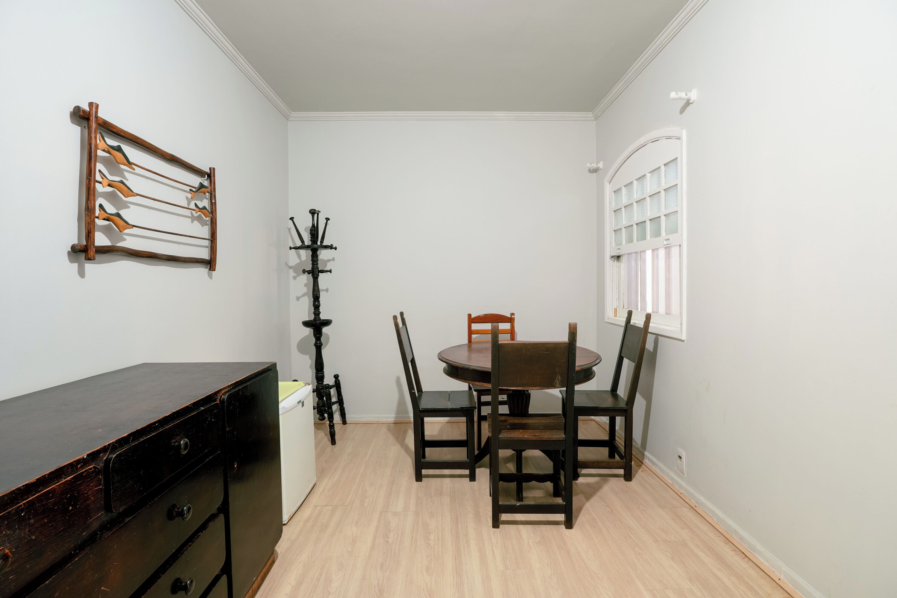 A dining area with a round table and four chairs, a wooden dresser, and a coat rack with coats.