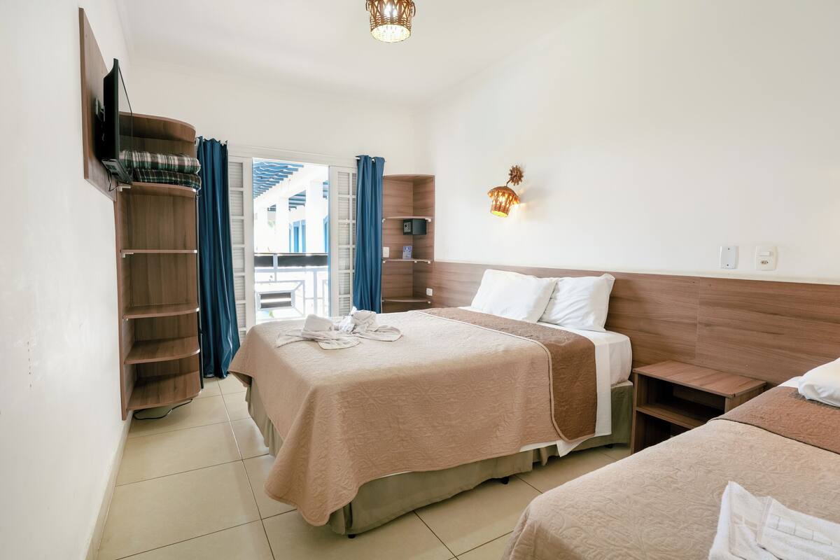 Habitación de hotel con cama, armario, mesita de noche, televisor montado en la pared y ventana con cortinas.