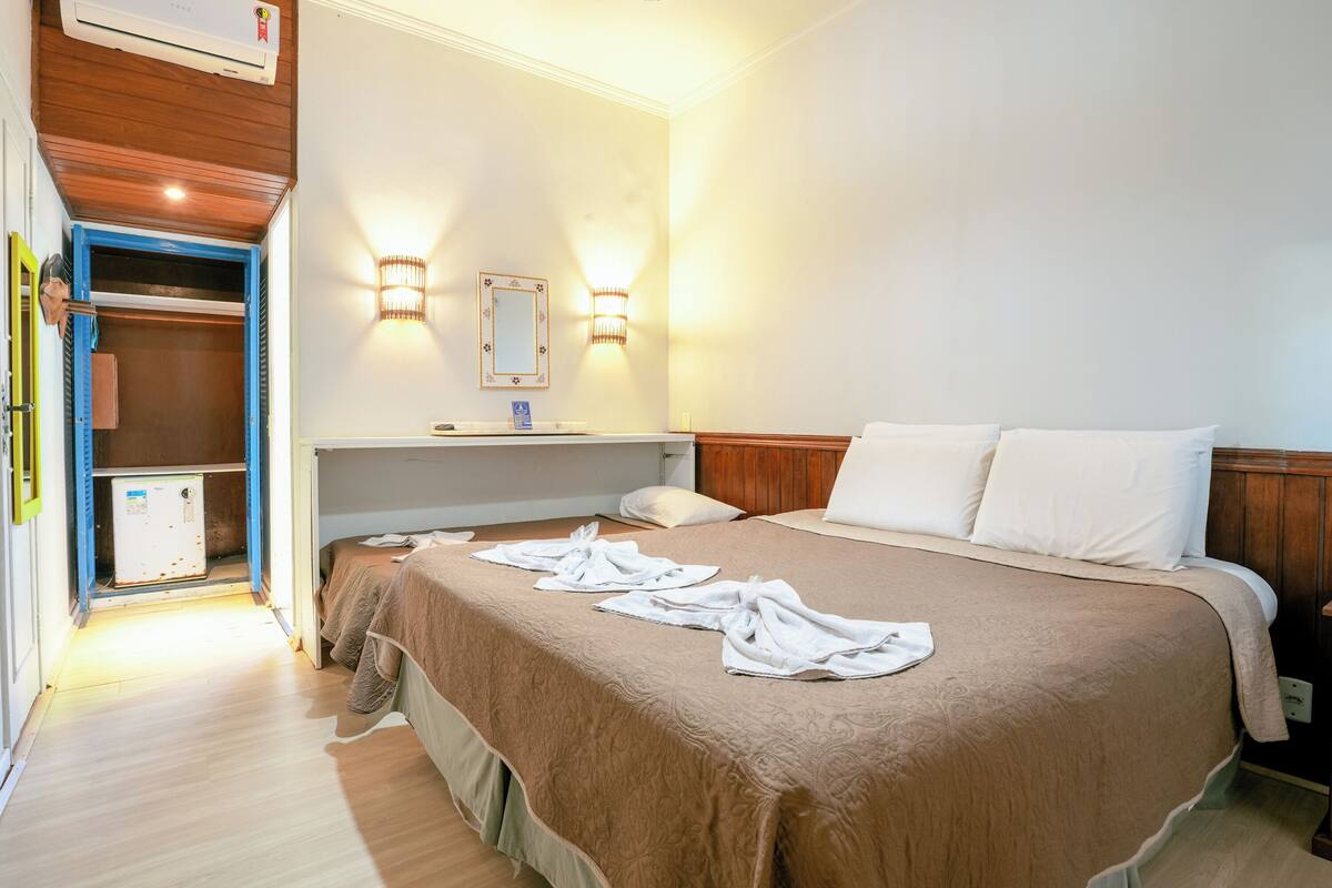 Una habitación de hotel con una cama grande, una mesita de noche, un espejo y un armario.
