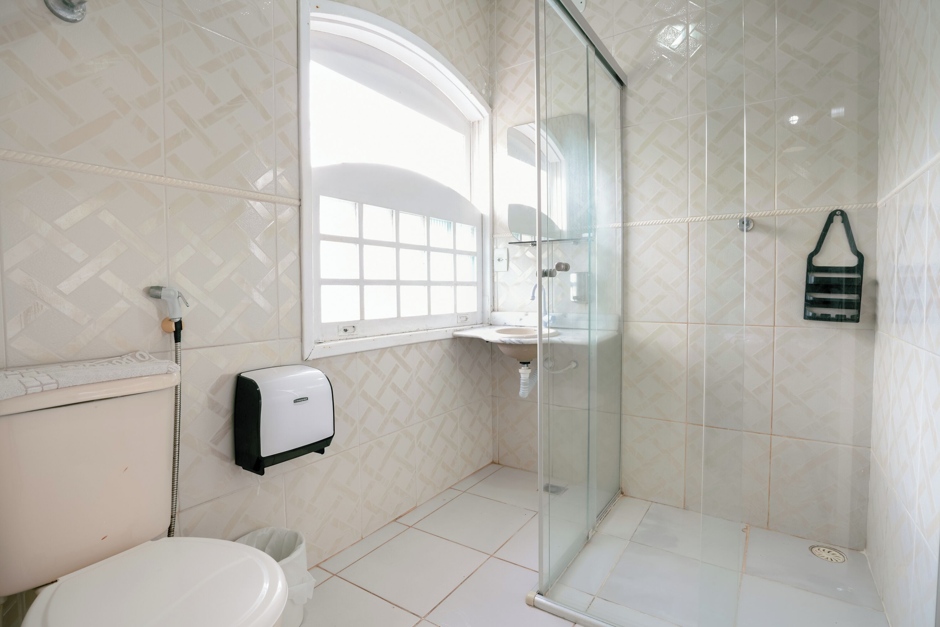 A bathroom with a toilet, a sink, a glass shower enclosure, and a window providing natural light.