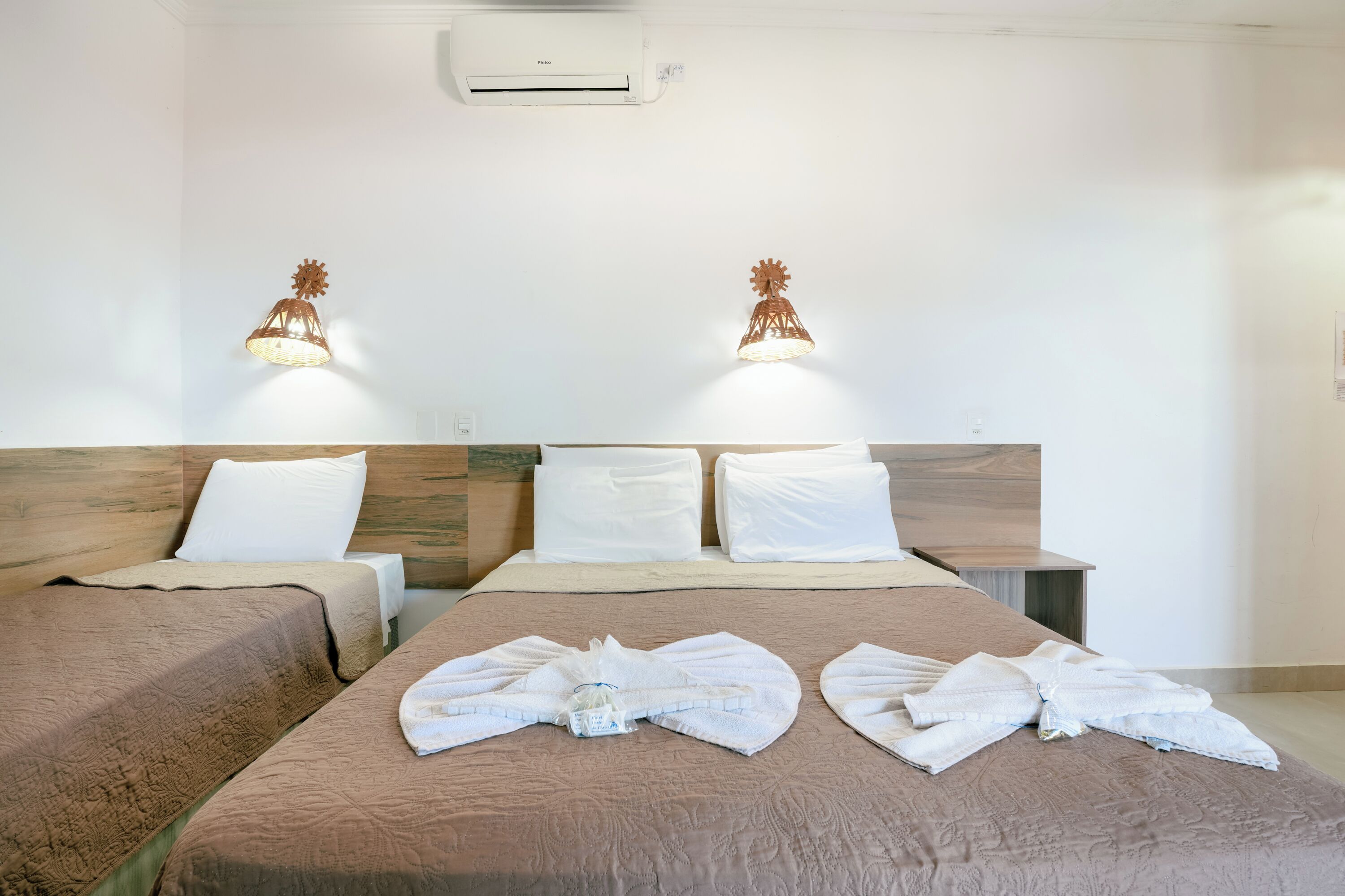 A hotel room with two beds, a wooden headboard, white linens, and two wall-mounted lamps.