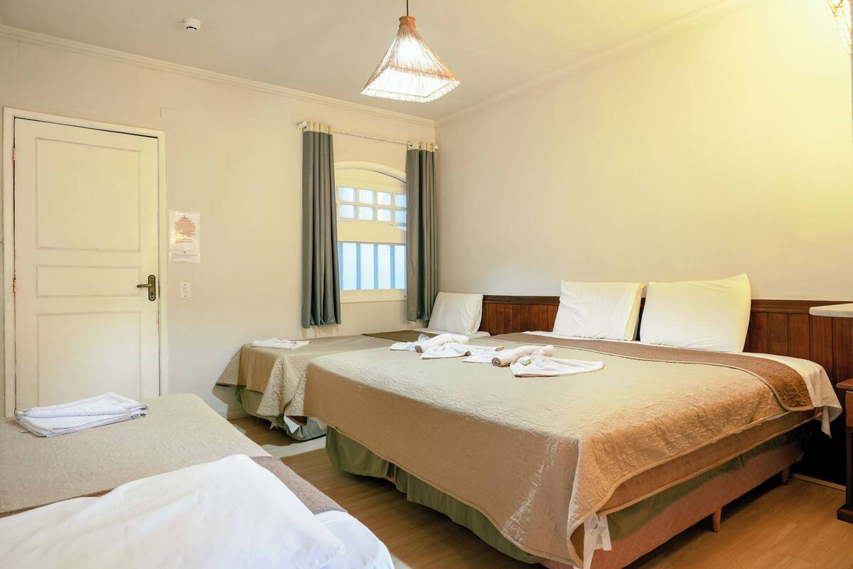Habitación de hotel con dos camas, una ventana con cortinas, una mesita de noche y una lámpara colgante.