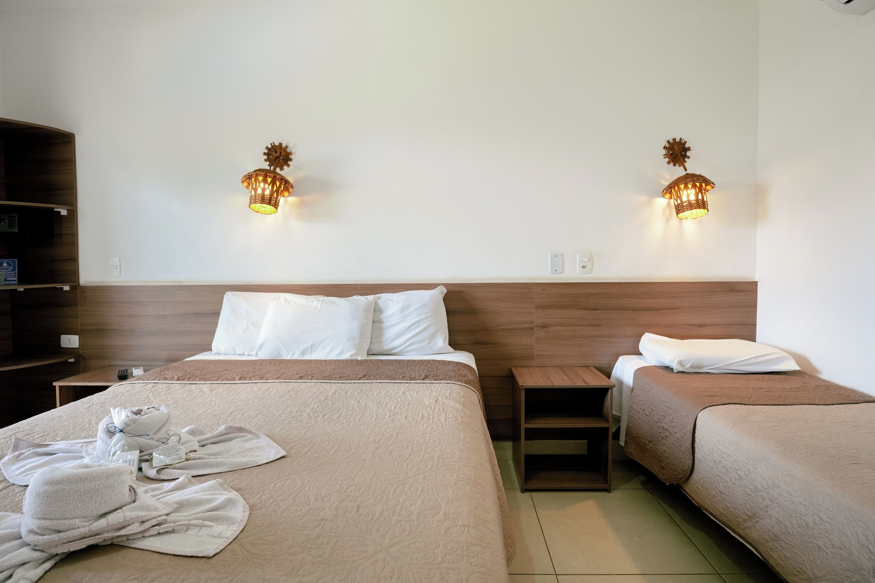 Habitación de hotel con dos camas, cabecero de madera, mesita de noche y dos lámparas de pared.