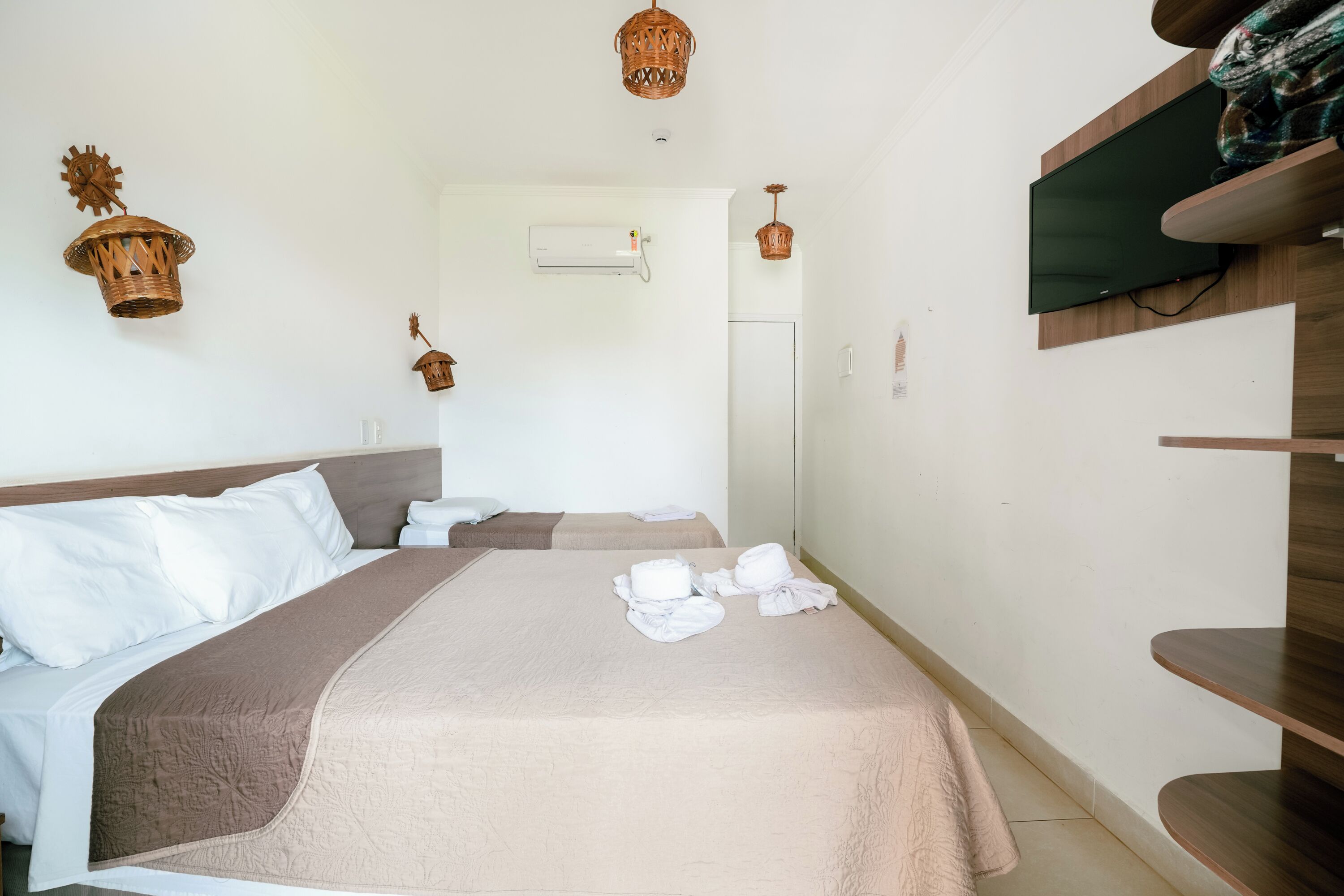 Habitación de hotel con una cama grande, un televisor montado en la pared y un pequeño estante con toallas dobladas.