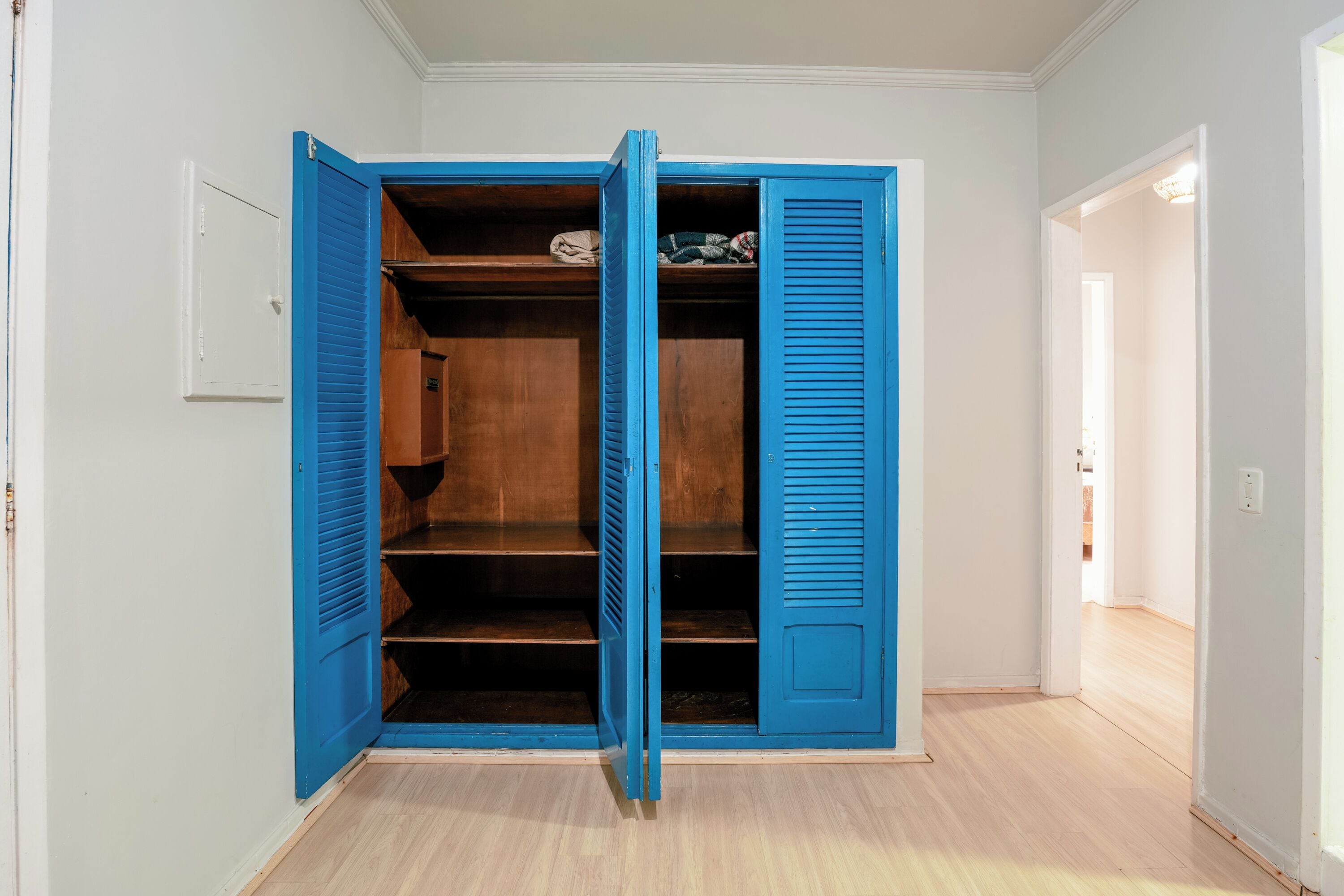 A walk-in closet with blue shutters, wooden shelves, and a white door.