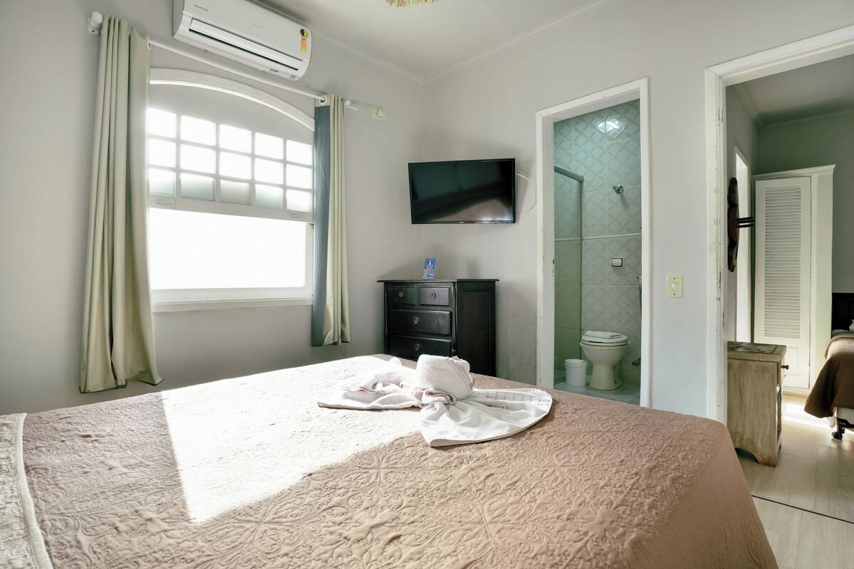 Una habitación de hotel con cama, televisión, baño con ducha y ventana.