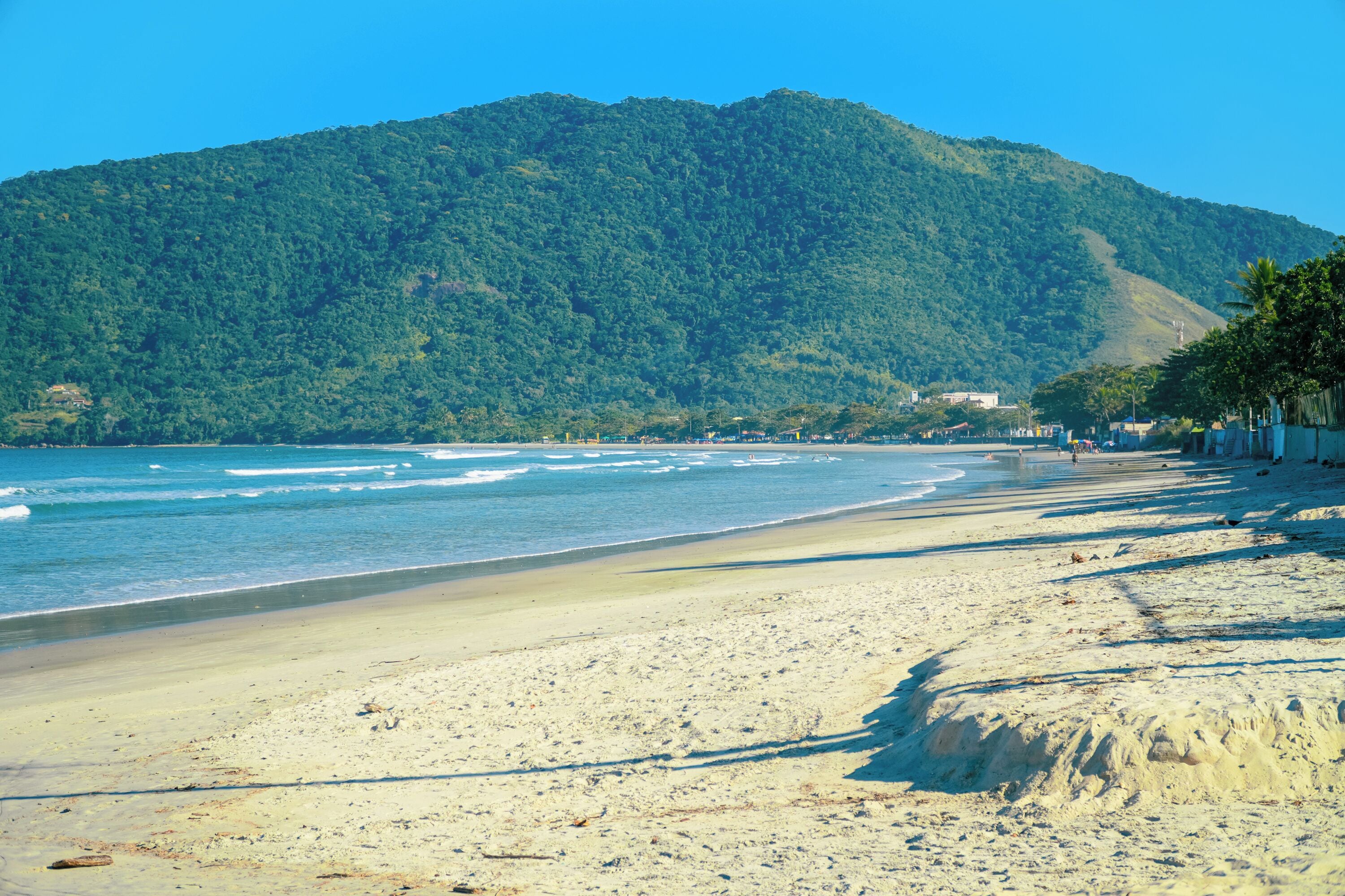 A beach with a mountain in the background, clear skies, and a calm sea.