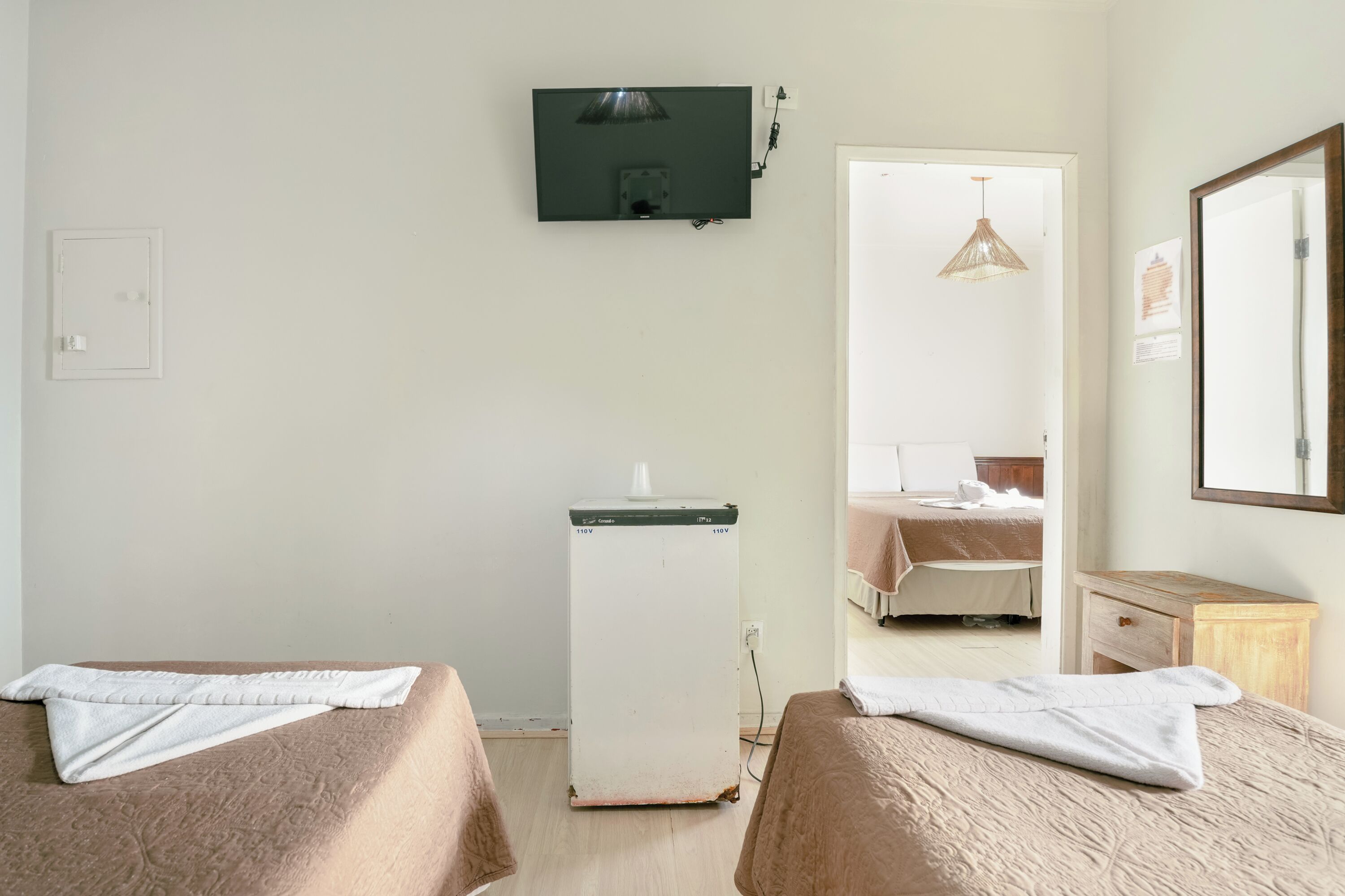 Une chambre d’hôtel avec deux lits, un petit réfrigérateur, une télévision et un miroir.