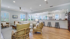 A spacious living area with a large window, a dining table, and wicker furniture. - Stunning bayside retreat with golf cart! (Captiva)