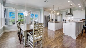 A spacious kitchen with a central island, white cabinetry, and a dining area with a wooden table and chairs. - Stunning bayside retreat with golf cart! (Captiva)