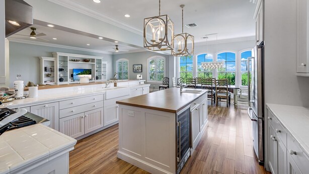 A spacious kitchen with white cabinetry, a central island, and a large window providing a view of greenery. - Stunning bayside retreat with golf cart! (Captiva)