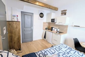 Et lille hotelværelse med seng, tekøkken, træskab og en dør.