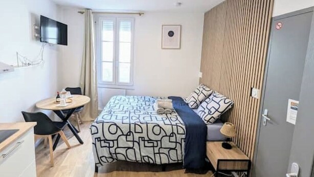 A compact hotel room with a bed, a small desk, a chair, a TV mounted on the wall, and a window with curtains. - Studio 1: Charm and convenience  (Gond-Pontouvre)