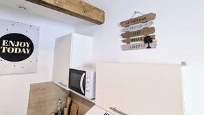 A kitchen with a wooden beam ceiling, a microwave, and a white refrigerator. There are signs on the wall with phrases like "ENJOY TODAY" and "LE VOYAGE EST LA PLUS BELLE LIBERTE." - Studio 1: Charm and convenience  (Gond-Pontouvre)