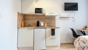 A compact kitchen with a microwave, coffee maker, and a small refrigerator. A flat-screen TV is mounted on the wall above the counter. - Studio 1: Charm and convenience  (Gond-Pontouvre)