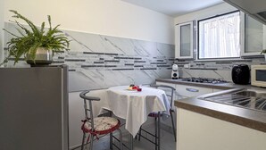 Et kompakt køkken med marmor bagvæg, et lille spisebord med stole, et køleskab, en mikrobølgeovn og en gasblus.