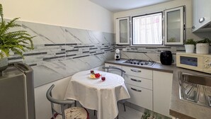 Et kompakt køkken med spisebord, stol, mikroovn, komfur og skabe.