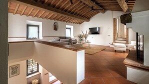 A spacious living area with a high ceiling, a staircase, and a flat-screen TV mounted on the wall. - Mulino Di Amarrante Countryhouse  (Montaione)