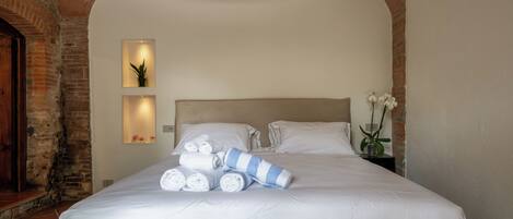 A neatly made bed with white linens and a striped towel, a wall-mounted light fixture, and a small potted plant.