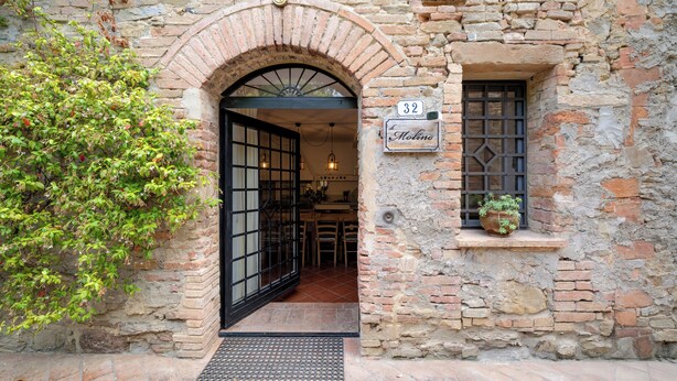 An entrance with a brick archway, a door with a metal grid, a window with a plant, and a sign with the number 32. - Mulino Di Amarrante Countryhouse  (Montaione)