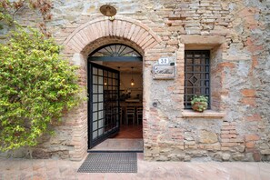 Une entrée surmontée d’une arche en briques, une porte avec une grille métallique, une fenêtre agrémentée d’une plante et une enseigne portant le numéro 32.