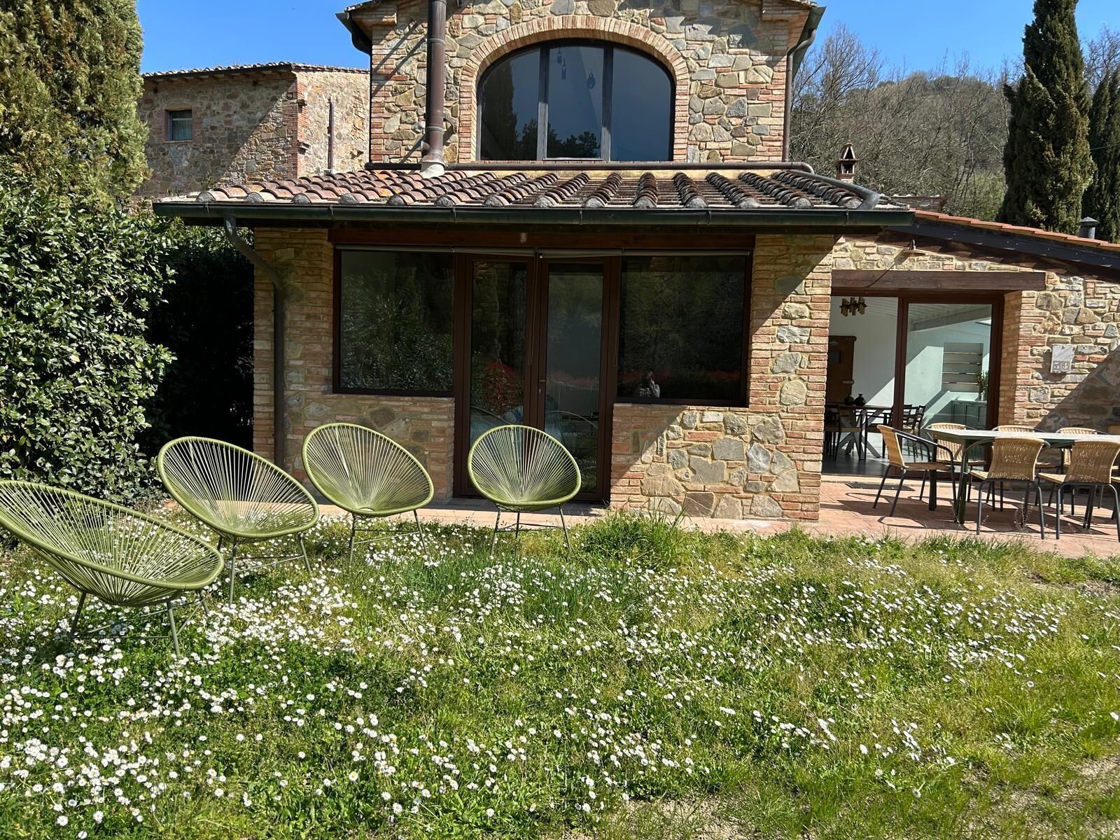 Un edificio in pietra con un'ampia finestra, un patio con sedie e un giardino.