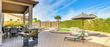 A patio with a grill, outdoor seating, and a swimming pool.