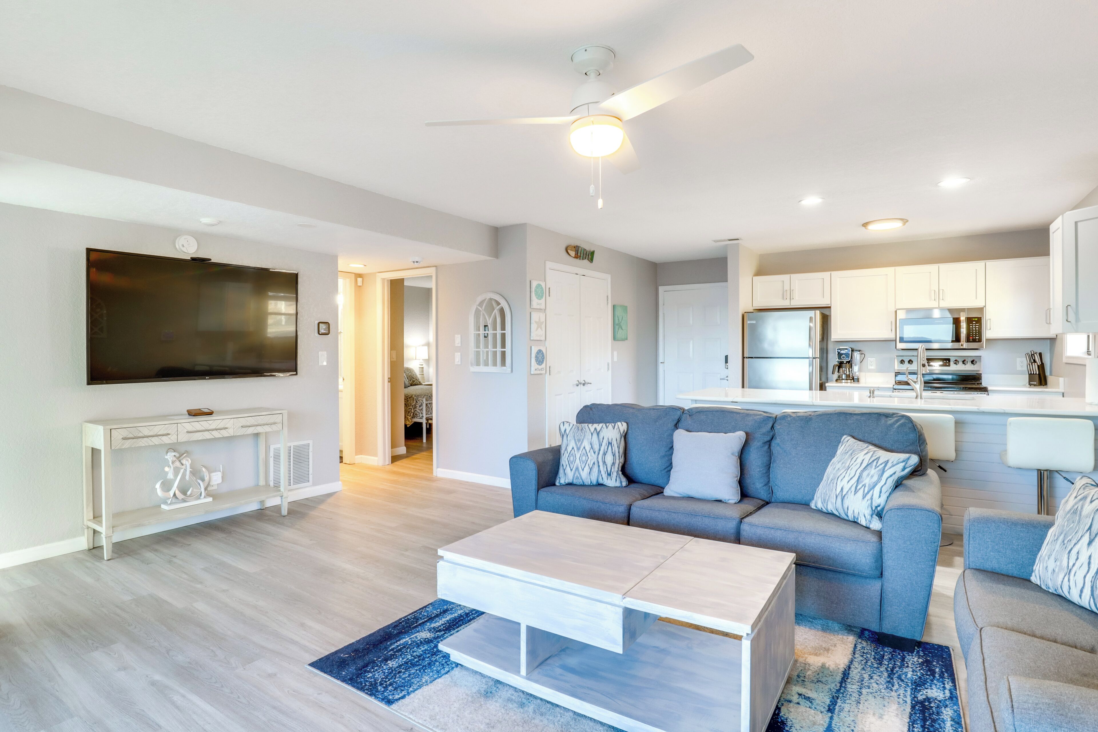 A modern living room with a grey sofa, a white coffee table, and a flat-screen TV mounted on the wall.