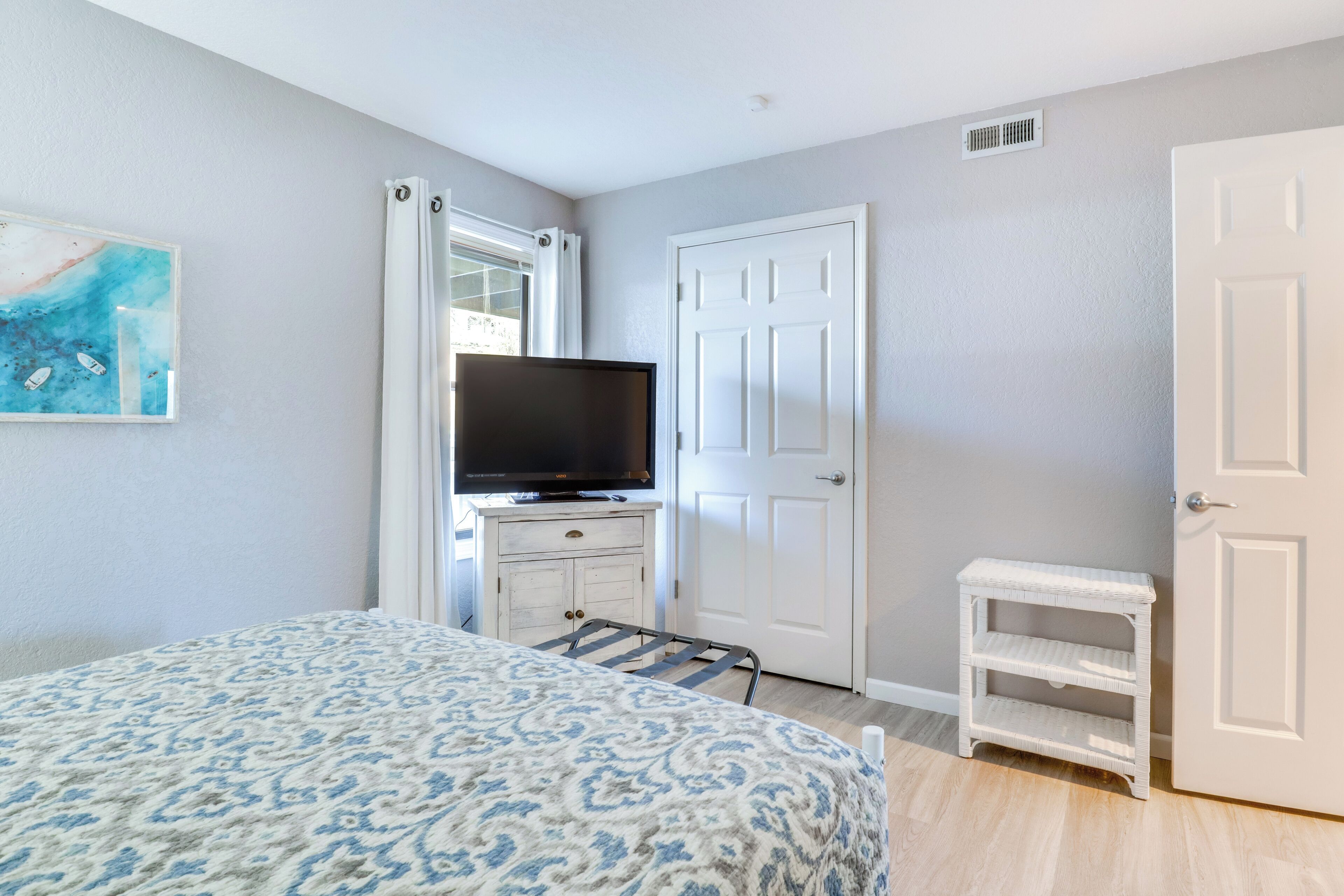 A bedroom with a bed, a television on a dresser, a door, and a small white shelf.