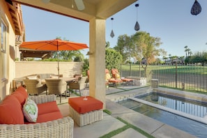 A covered outdoor seating area with wicker furniture and an orange umbrella, a swimming pool, and a view of a golf course. - 2 Mi to Coachella Grounds: Home w/ Fire Pit! (Indio)