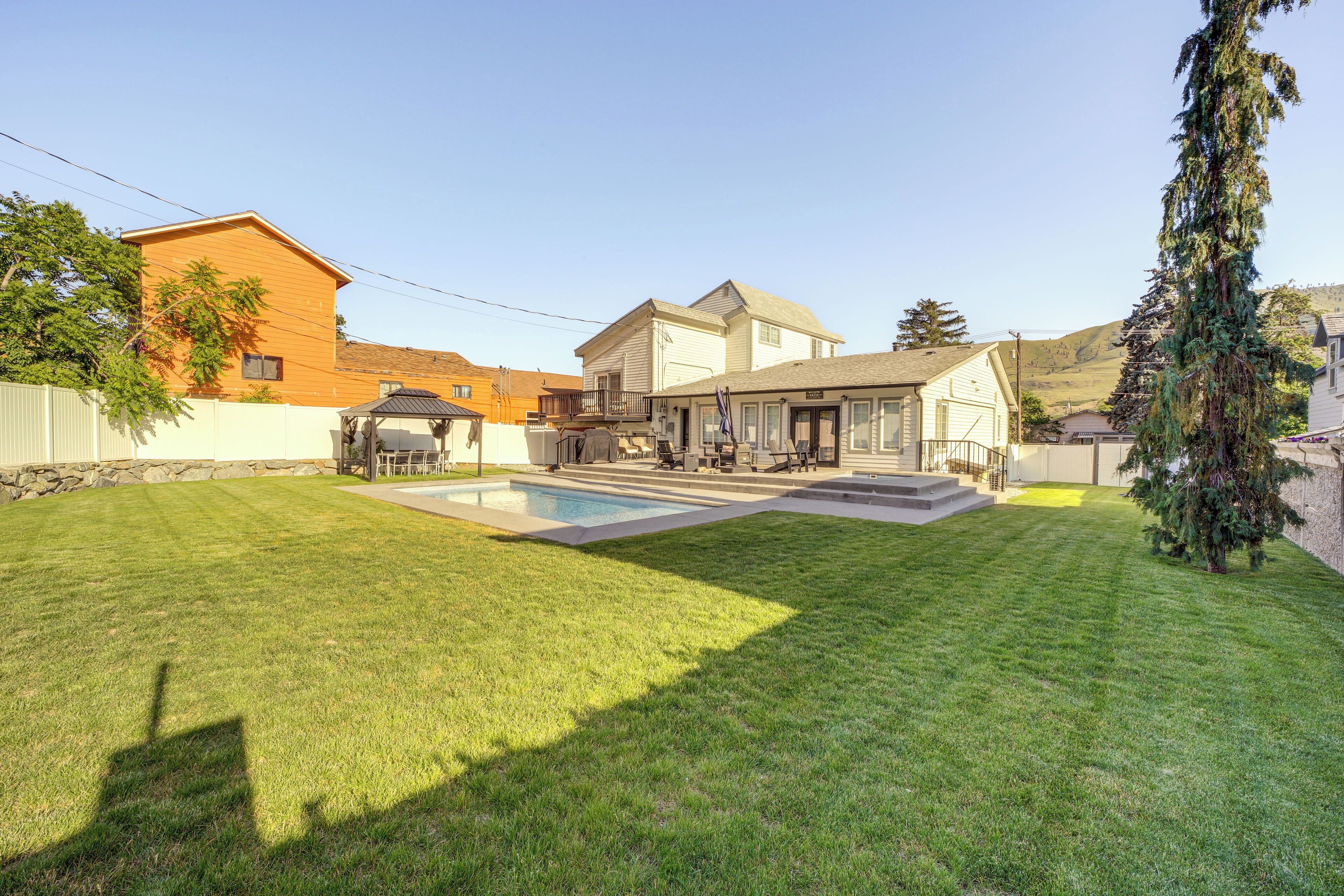 Un jardin arrière d’une maison, avec une piscine, un patio couvert et une pelouse bien entretenue.
