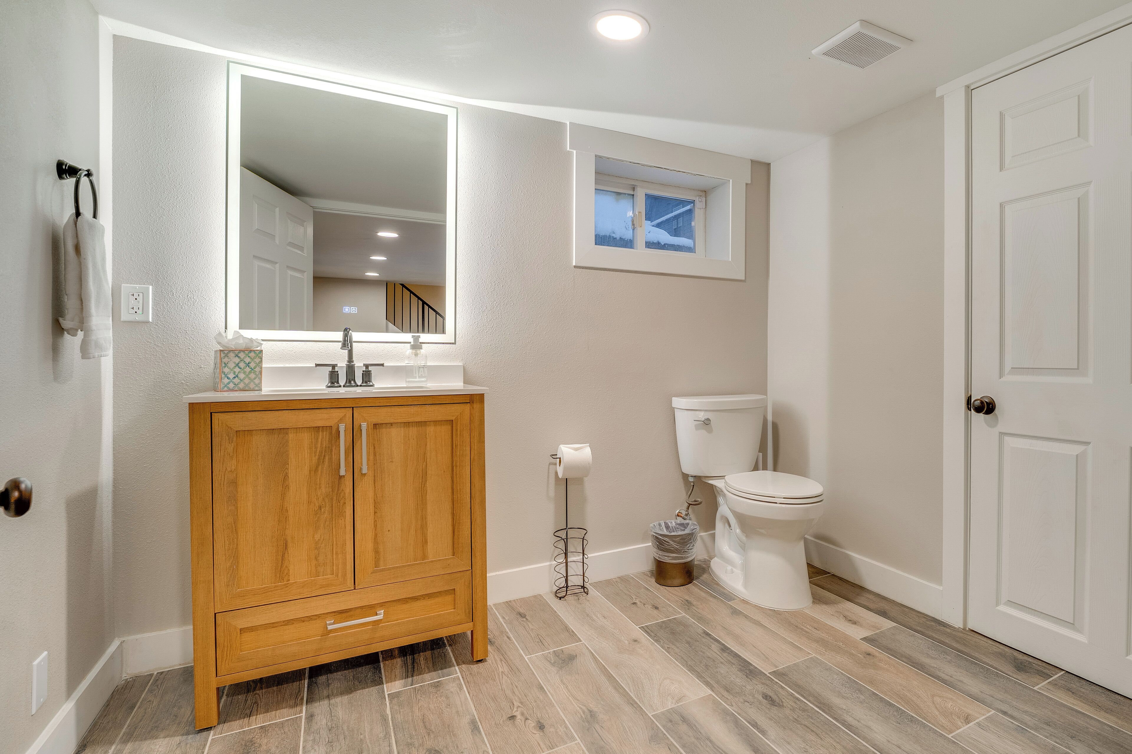 A bathroom with a wooden vanity, a large mirror, a toilet, and a window.