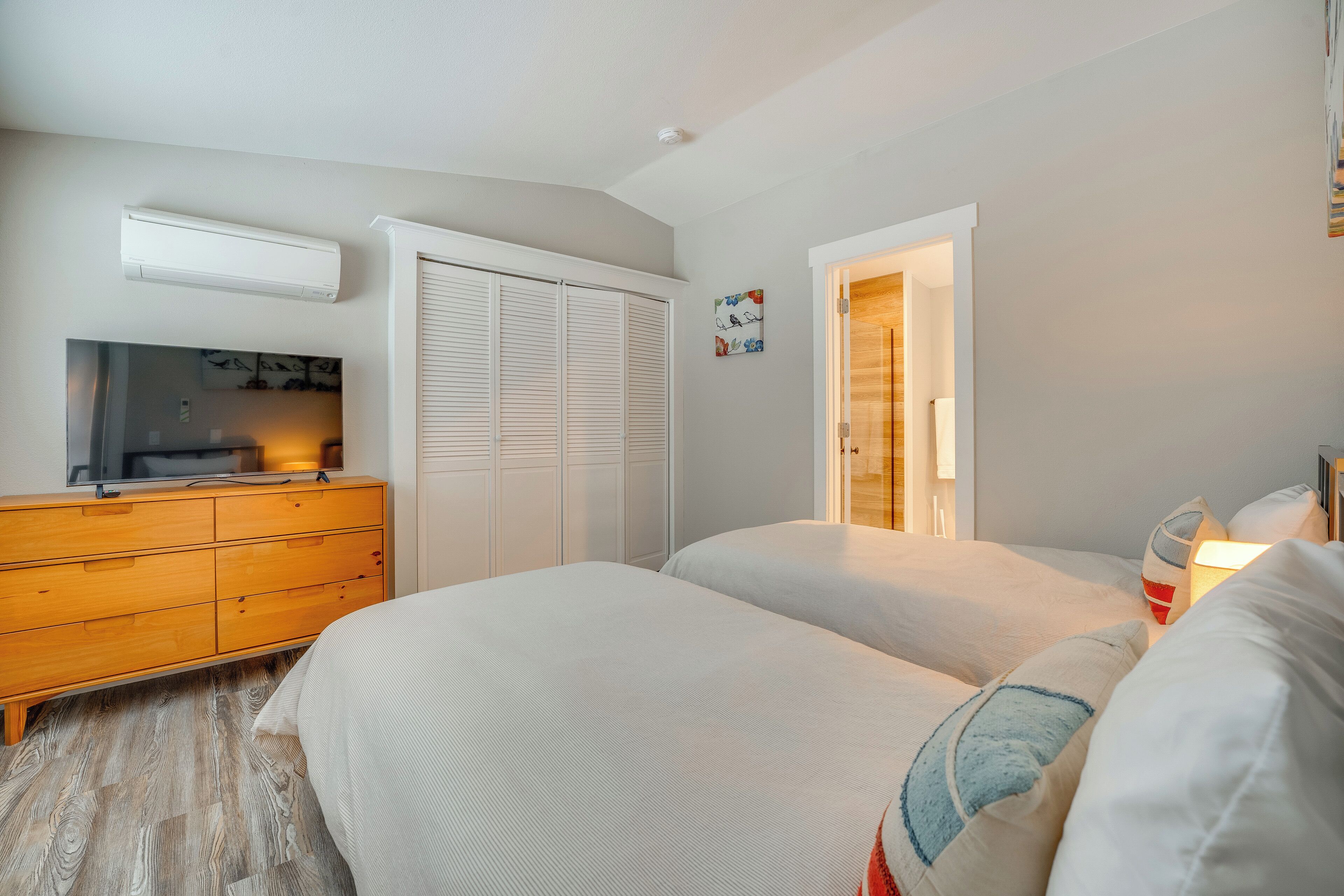 Une chambre avec deux lits, une commode en bois, une télévision et un placard.