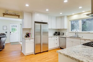 A modern kitchen with white cabinets, a stainless steel refrigerator, a coffee maker, and a large window. - Fire Pit + Grill: Retreat Between Arnold & Murphys (Avery)