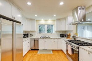 A modern kitchen with white cabinets, stainless steel appliances, a window, and a wooden floor. - Fire Pit + Grill: Retreat Between Arnold & Murphys (Avery)
