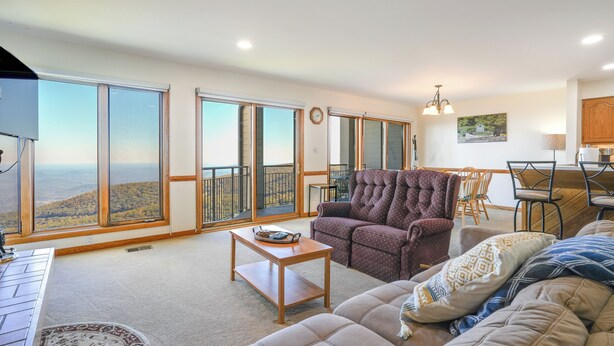 A spacious living room with a large window, a sofa, a coffee table, and a dining area with chairs. - 1 Mi to Wintergreen Resort: Mtn-view Condo! (Nellysford)