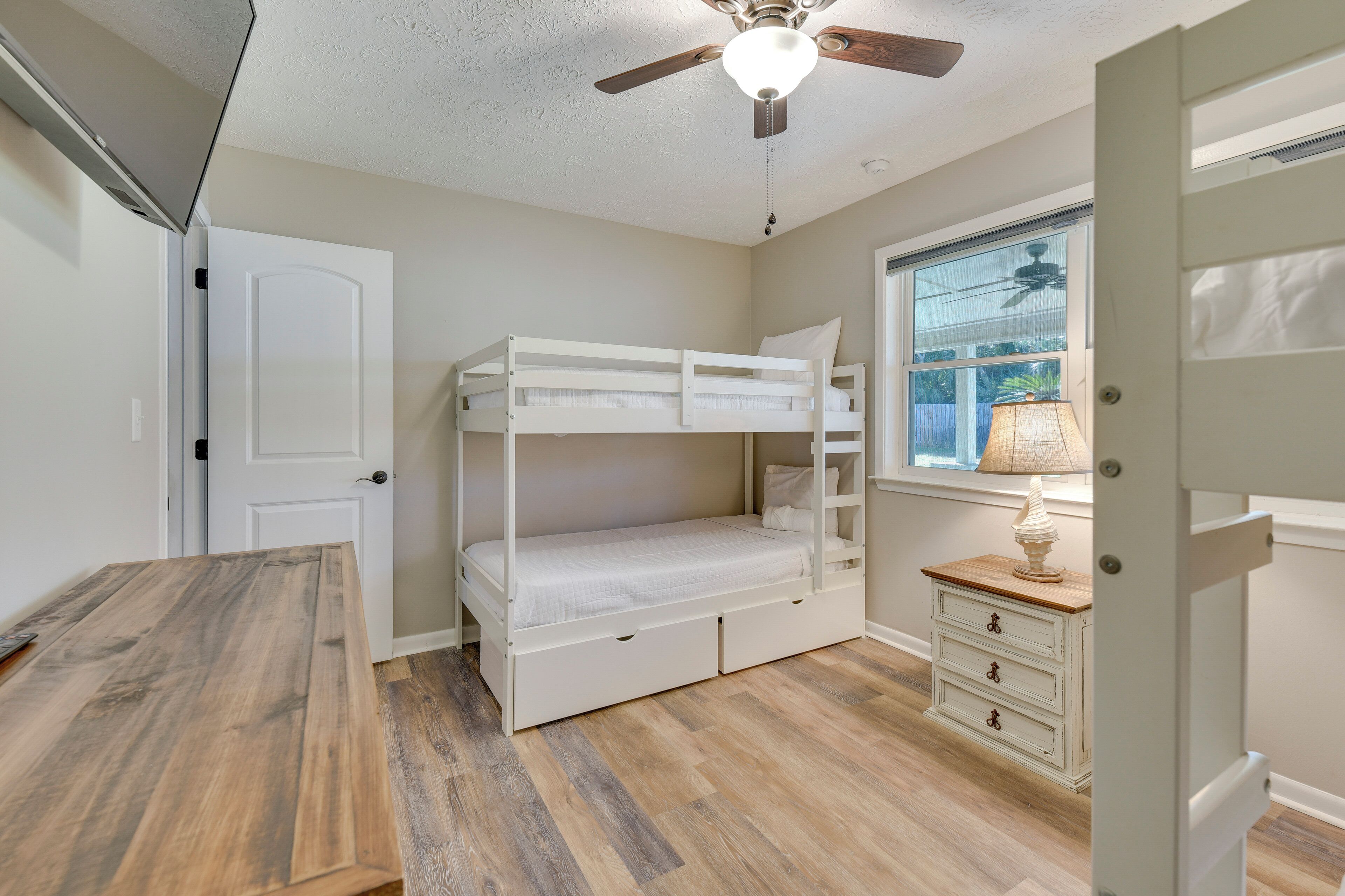 Une chambre avec un lit superposé, un bureau en bois, une commode et une fenêtre donnant sur un paysage verdoyant.