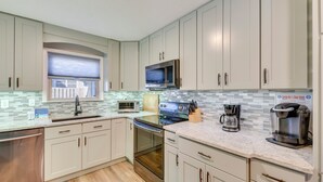 A modern kitchen with light-colored cabinets, a stainless steel dishwasher, a built-in oven, a microwave, and a coffee maker. - Walk to Gulf: Tranquil Home w/ Yard in Pcb! (Panama City Beach)