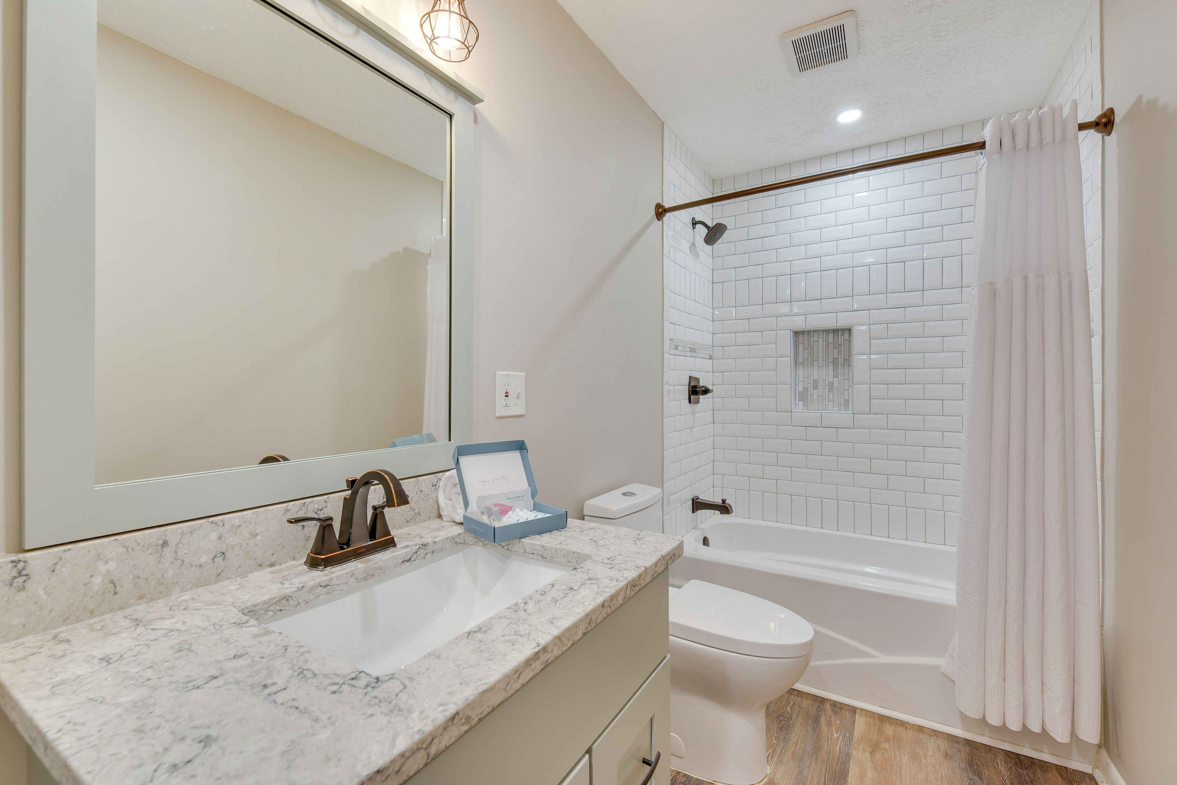 A bathroom with a marble sink, a toilet, a bathtub, and a shower curtain.