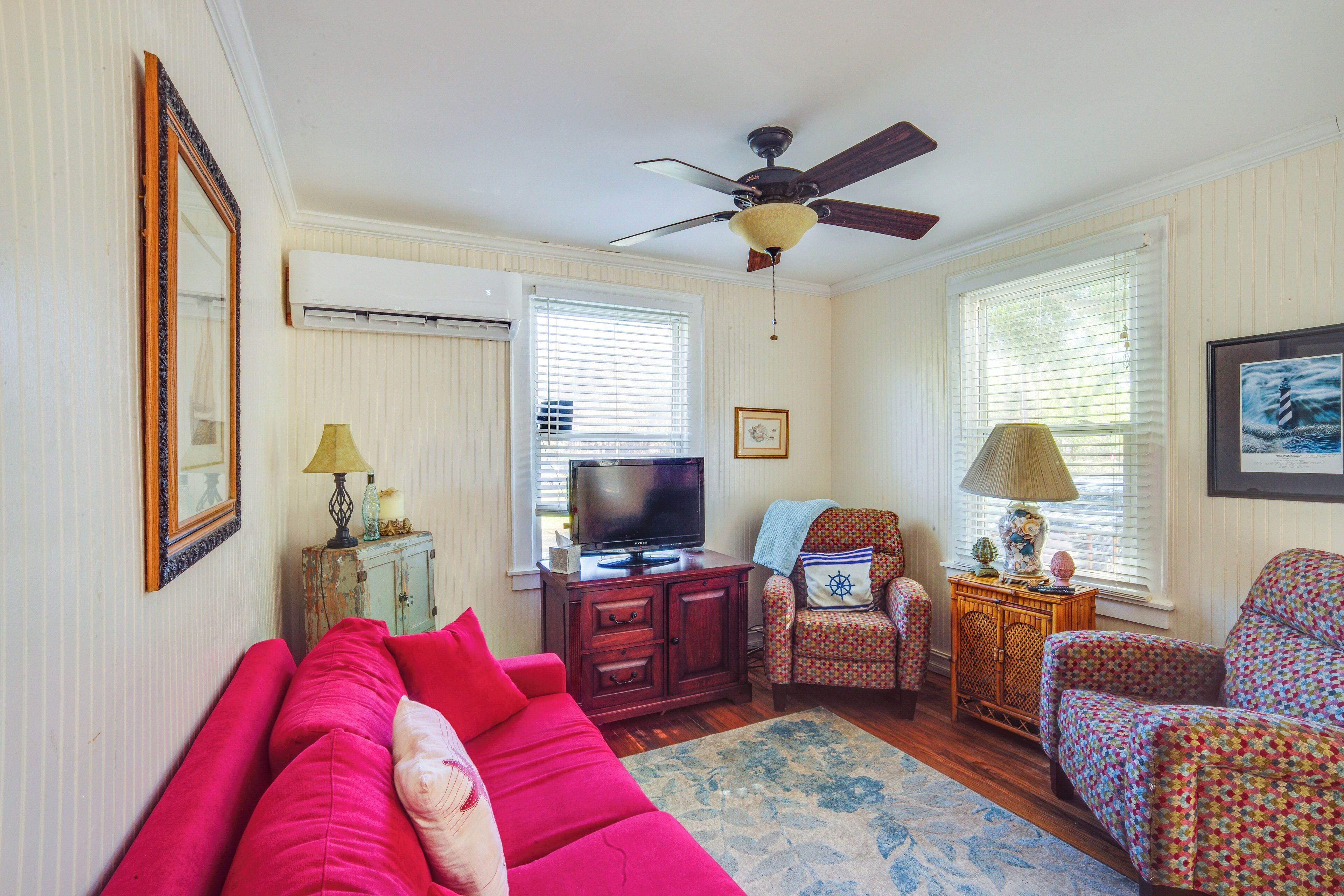 A living room with a red sofa, a television, a ceiling fan, and a patterned armchair.