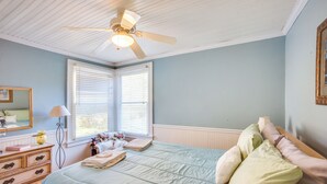 Un dormitorio con cama, cómoda, espejo, ventana y ventilador de techo.