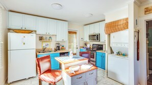 Una cocina compacta con electrodomésticos blancos, armarios azules y un comedor con mesa y sillas.