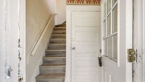 Una escalera que conduce a una puerta blanca con pomo de latón y un ventanal pequeño.