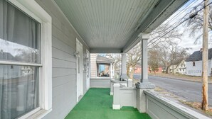 En inglasad veranda med ett golv av grön konstgräsmatta, vita räcken och utsikt över gatan och de intilliggande husen.